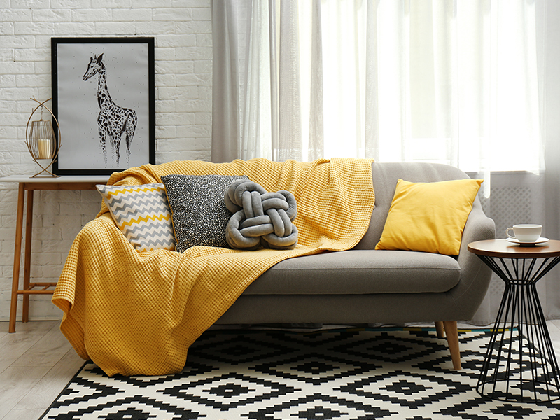 Graues Sofa mit gelber Decke - Pantone Trendfarbe 2021